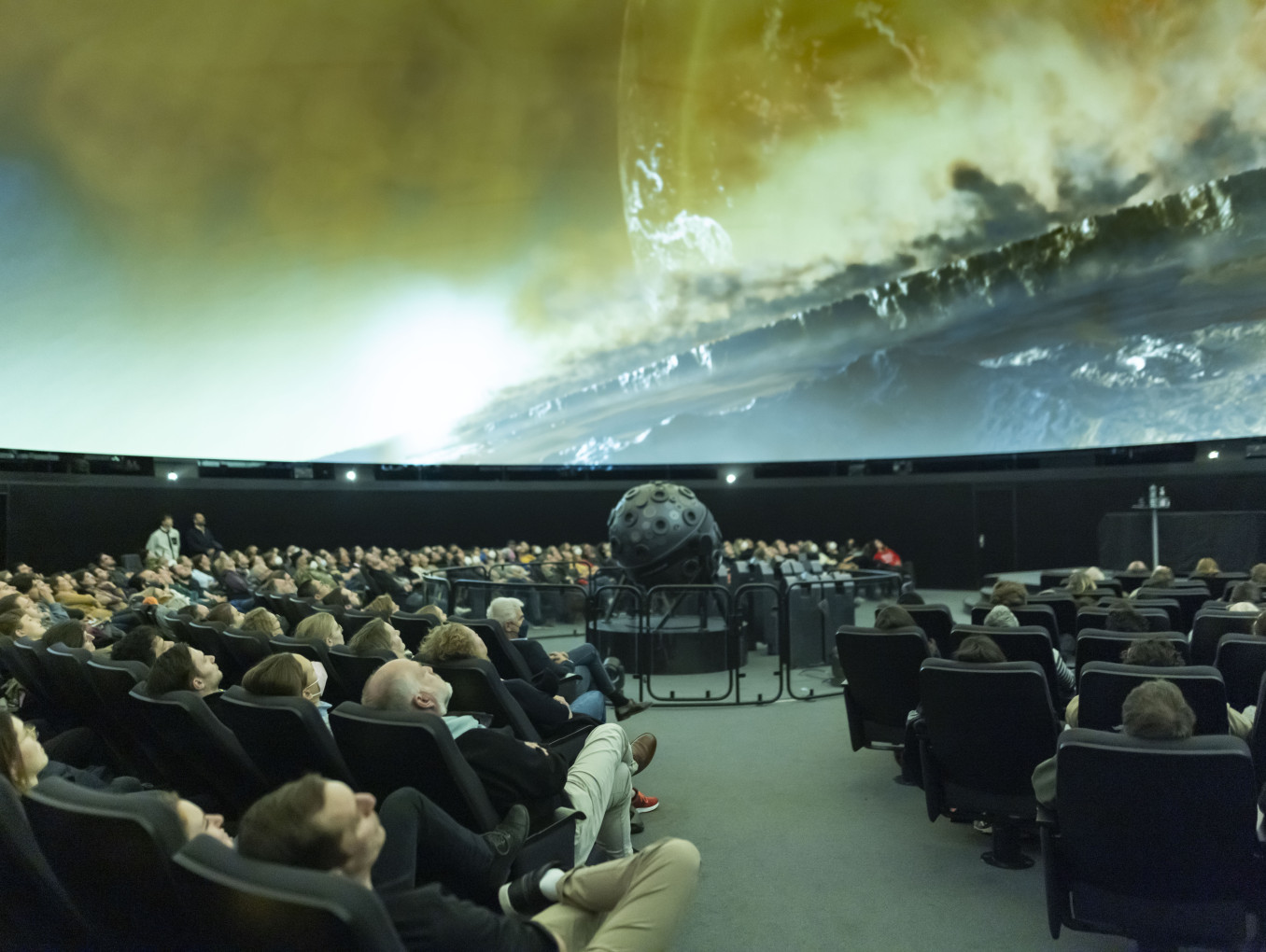 A picture of people in a planetarium, watching a screen in front and above them.
