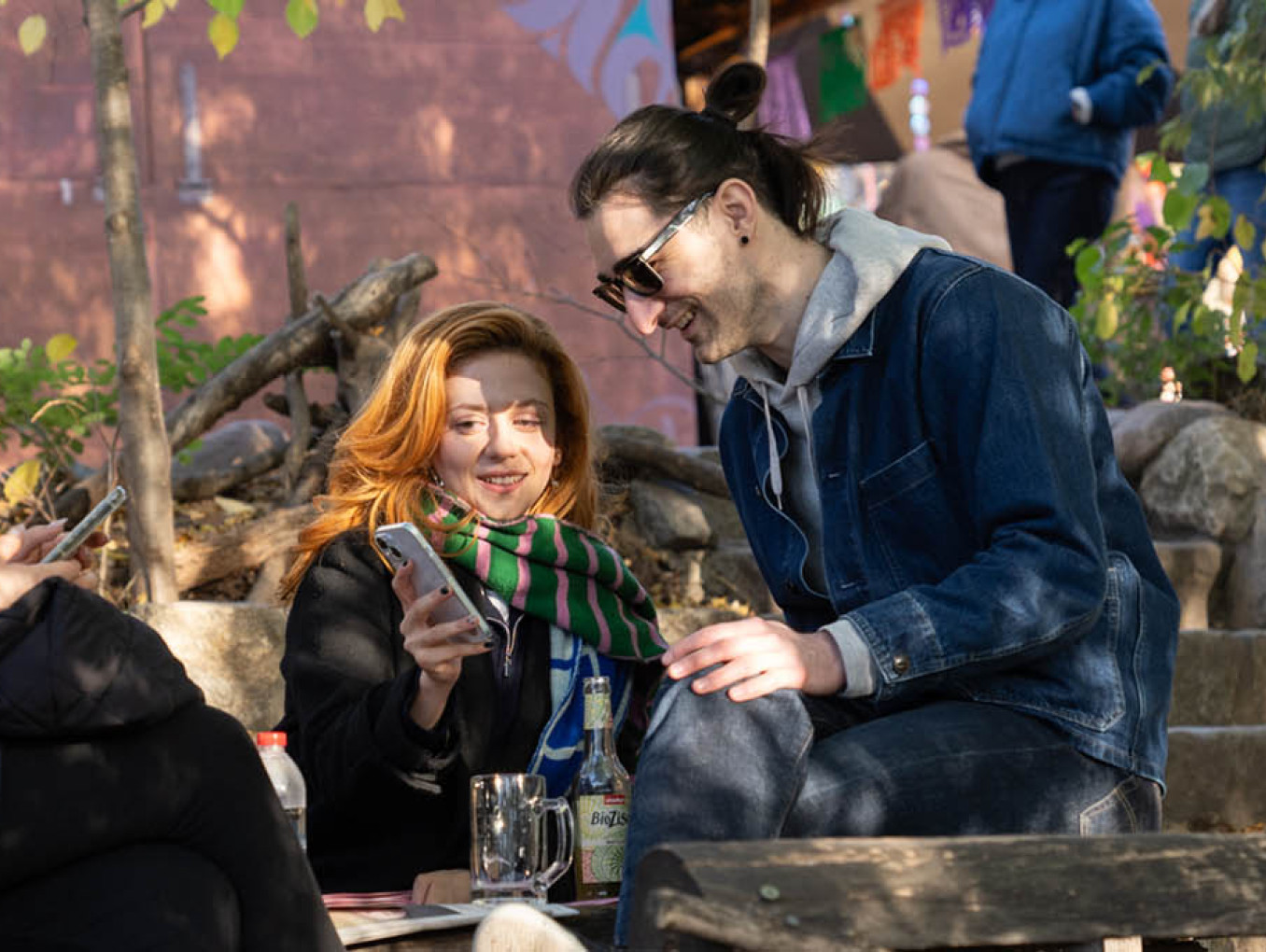 Three people seated outside looking at newsletters on their phones.