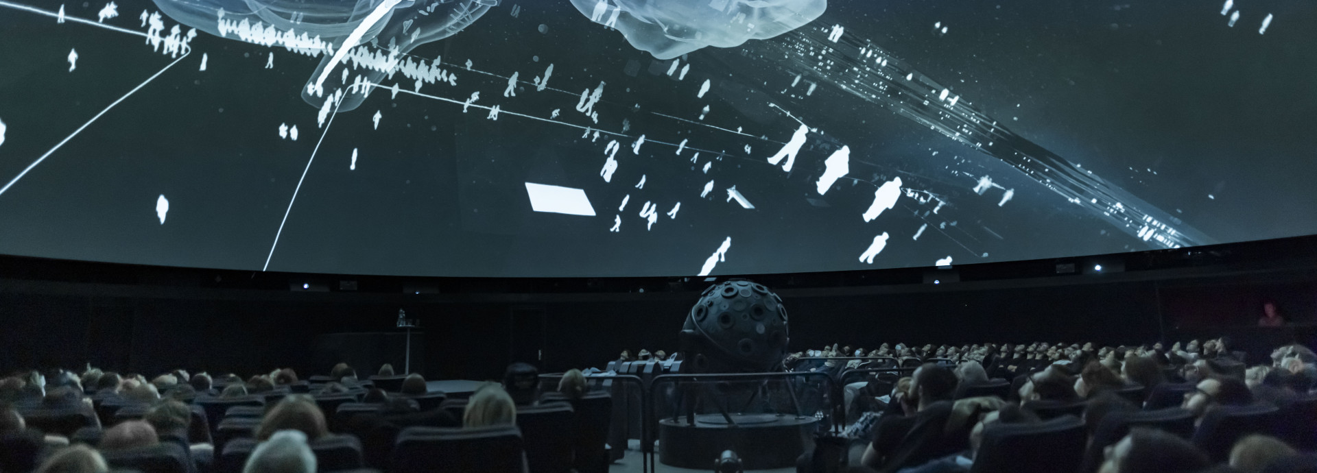 Room shot of people in a planetarium watching a projection on the ceiling