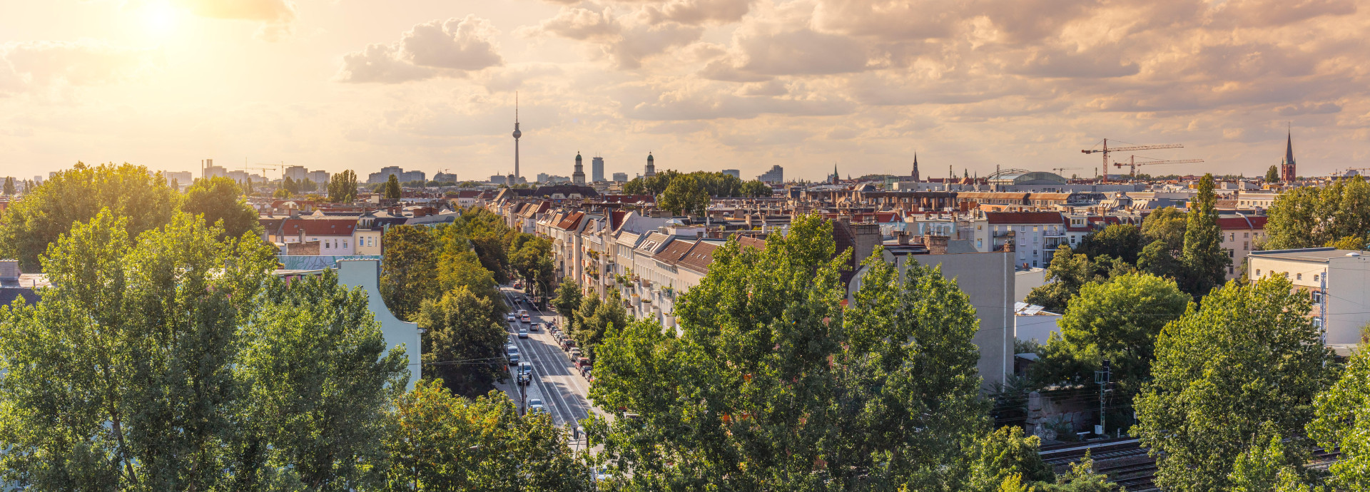 Panorama-Ansicht von Berlin, grün blühende Bäume, vereinzelte Wolken, während die Sonne untergeht