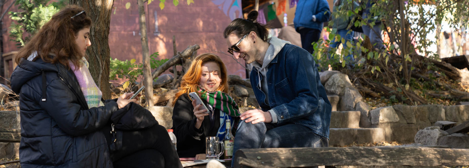 Three people seated outside looking at newsletters on their phones.