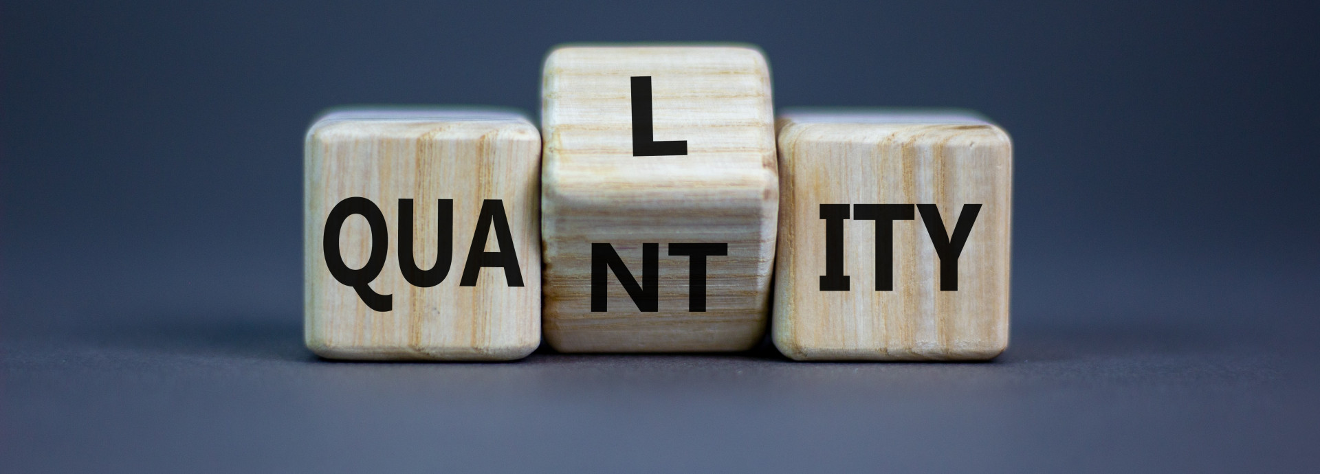 A picture with wooden letters which are simultaneously spelling "Quality" and "Quantity".
