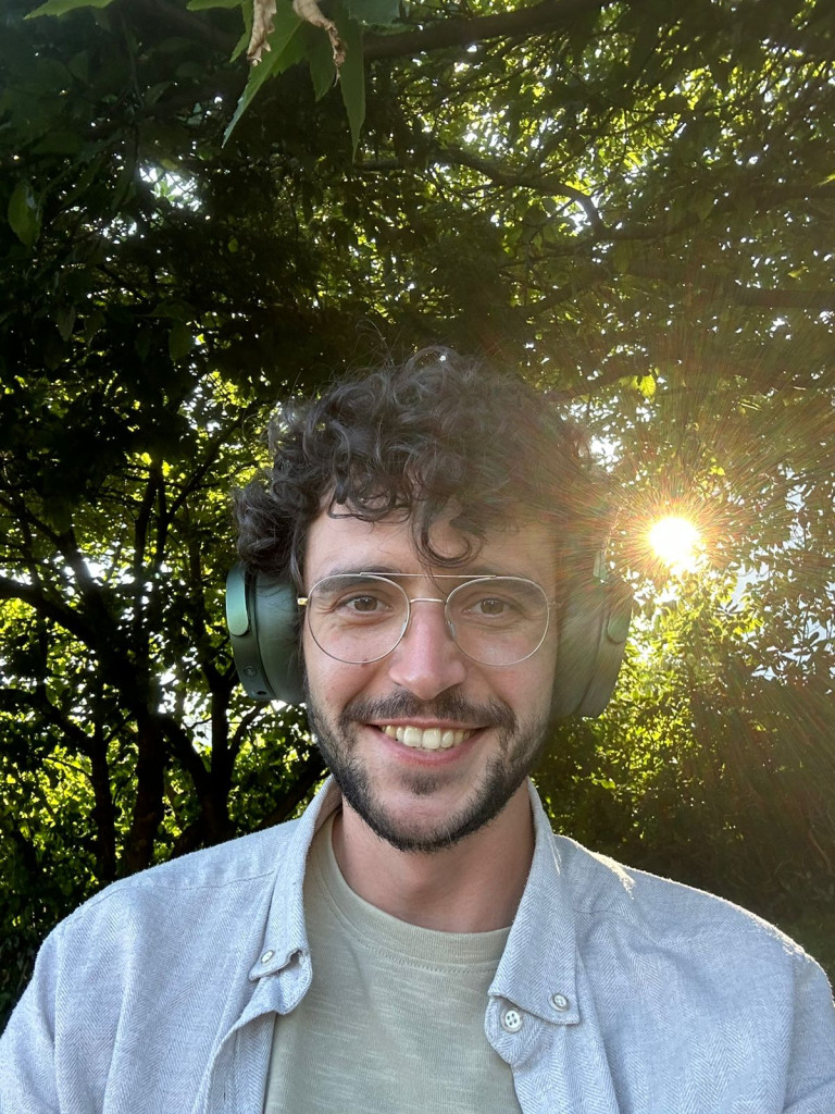 Selfie of Artem Filipenko, smiling, wearing green headphones. In the background, the sun shines through the trees.