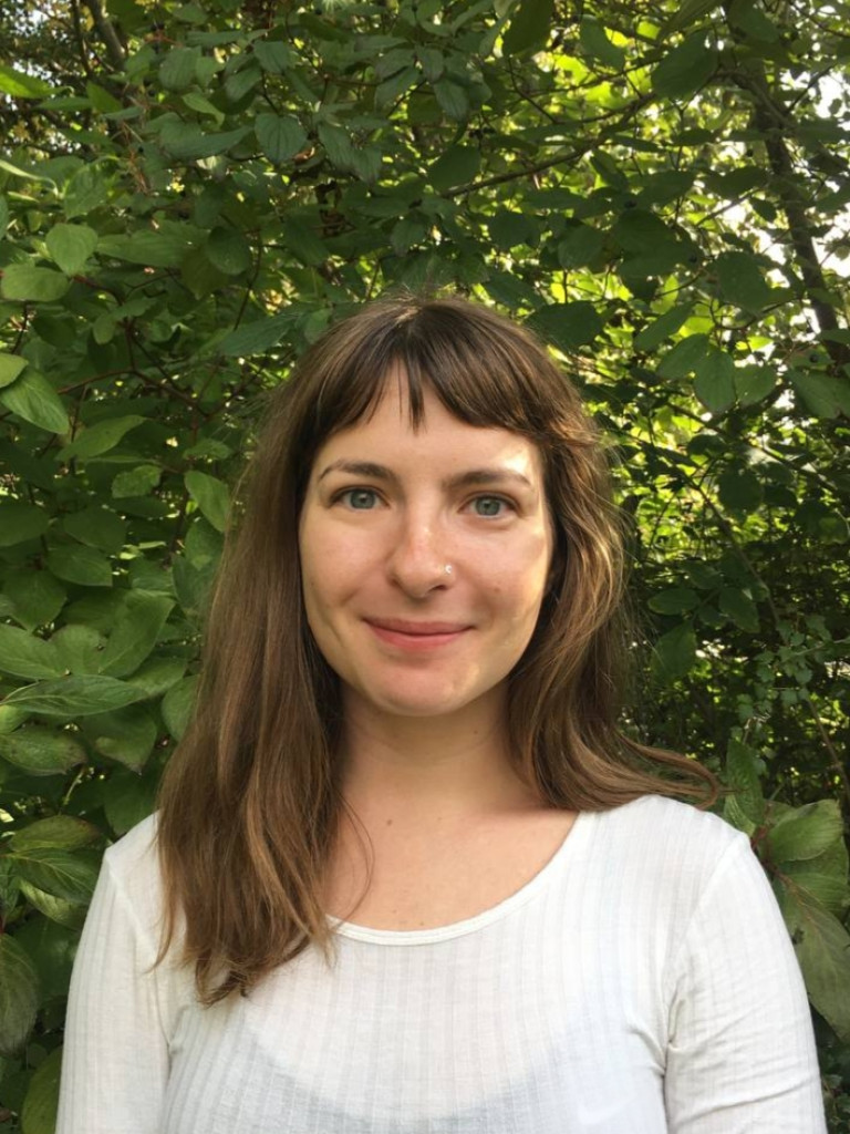 Eleanor Percy-Rouhaud wearing a white top and slighty smiling, with lush greenery in the background.