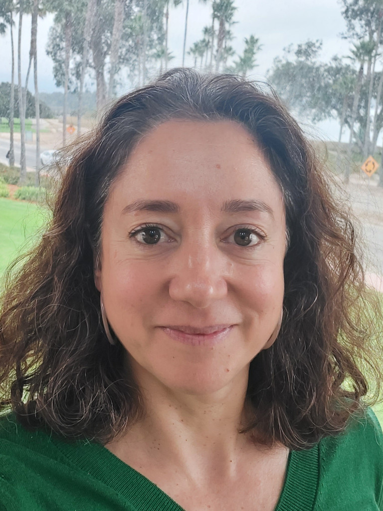 Livia de Hoz headshot. She is wearing a green top, and there are trees in the background.