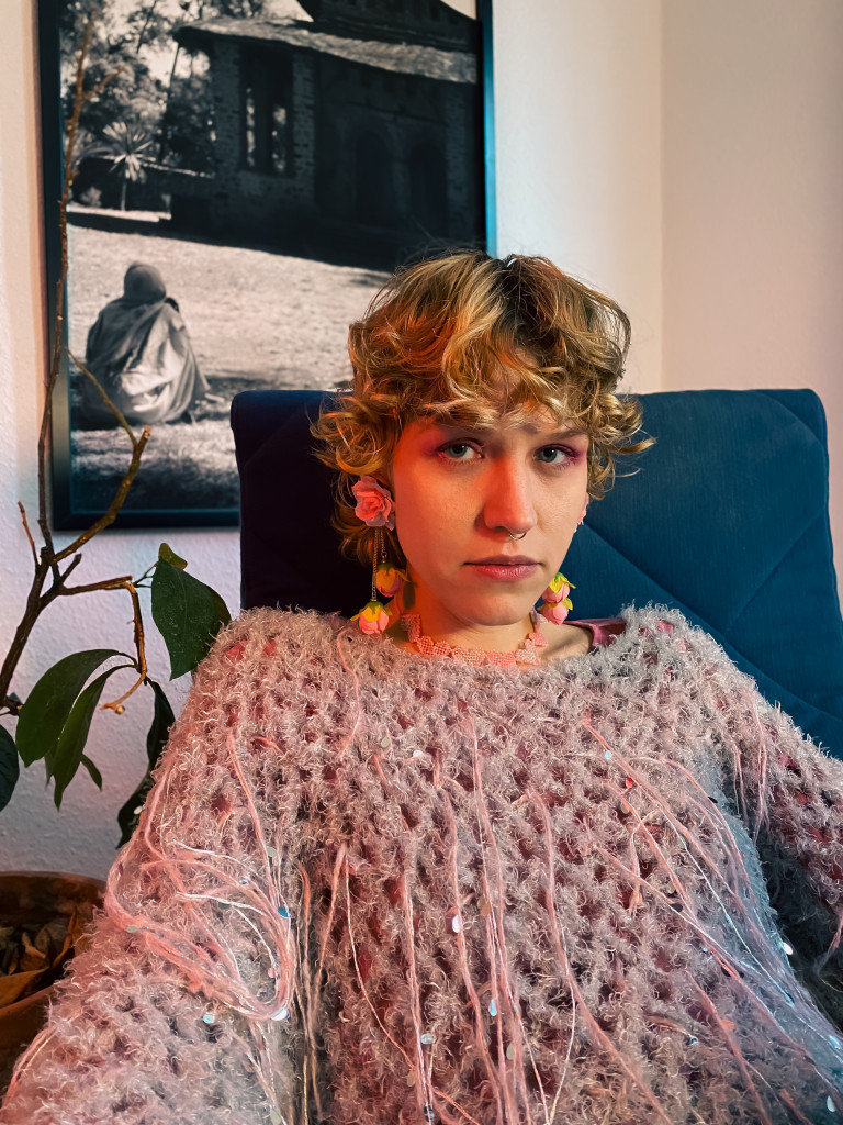 Sveta Gorlatova sitting on a blue chair in a living room or office. There is a framed black & white photograph hanging on the wall behind them.
