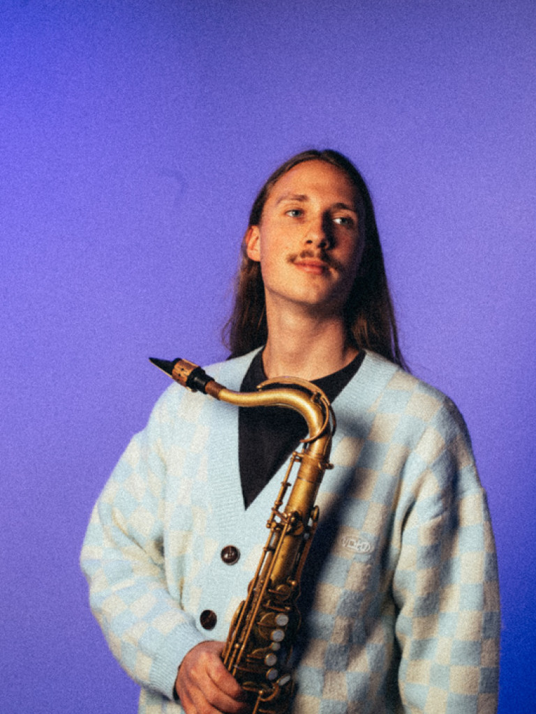 Daniel Sauer holding a Saxophone in front of a purple background.