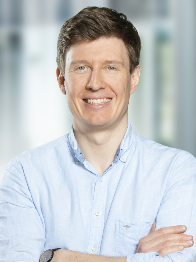 Portrait of Lukas Grünhaupt, a white male, wearing a light blue shirt, looking straight into the camera with his arms crossed