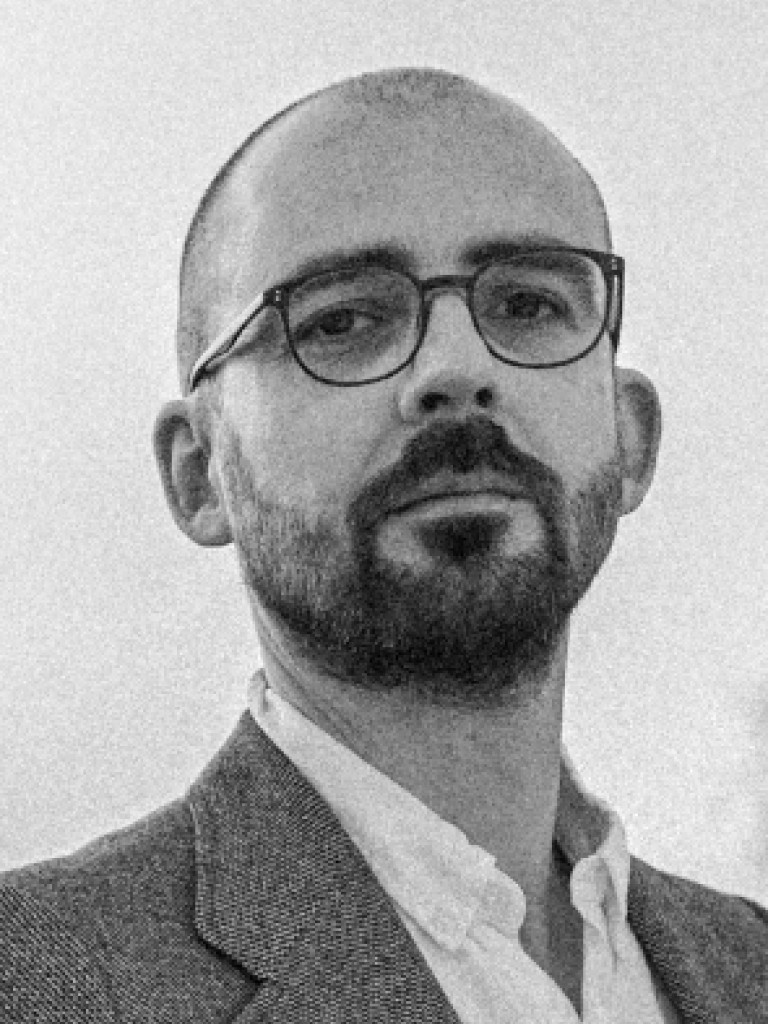 Black and white portrait Thomas Tichai, a white male in his forties with short dark hair, glasses and a beard 
