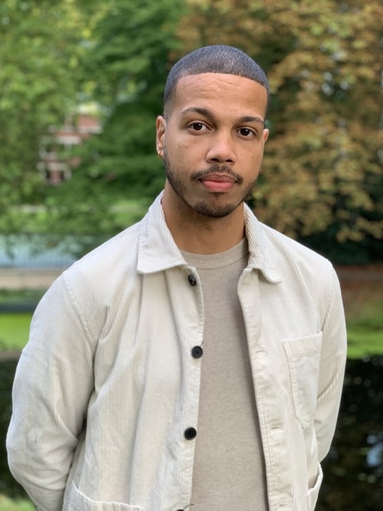 Daudi van Veen wearing a beige t-shirt and a lighter beige jacket while posing in a park