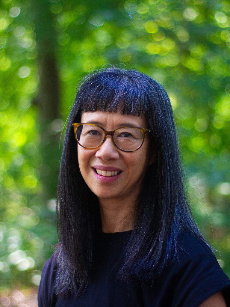 Linda Juang wearing a black shirt and reading glasses while posing to the camera in a park 