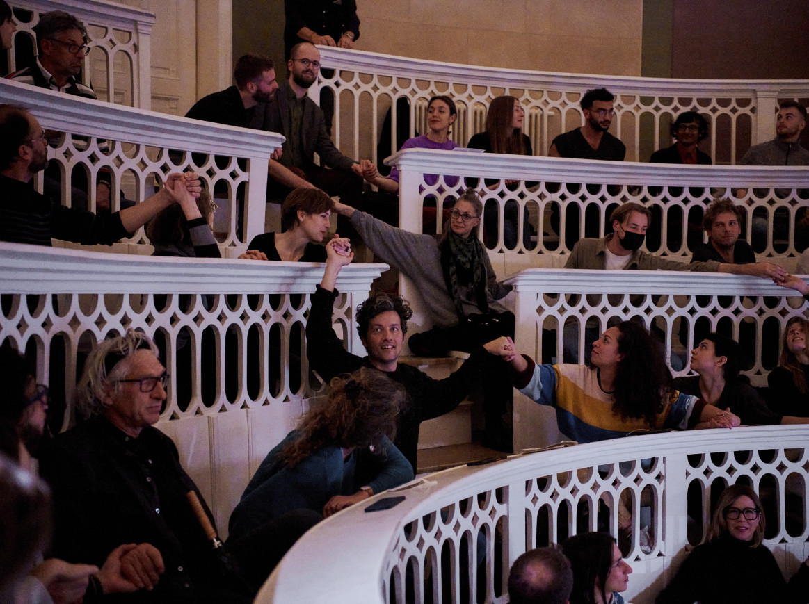 A shot of people holding hands across the rows of a white auditorium