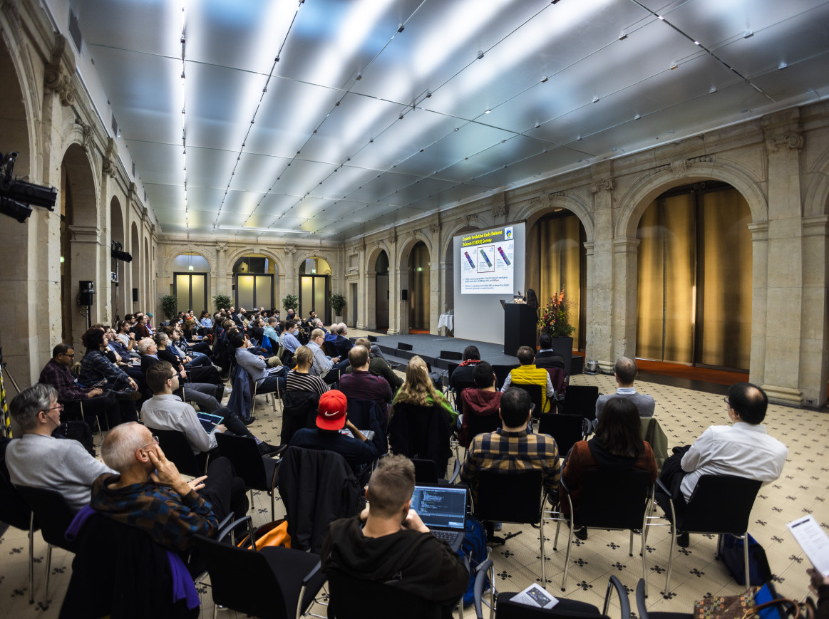 A wide shot of people sitting down and watching a talk on stage