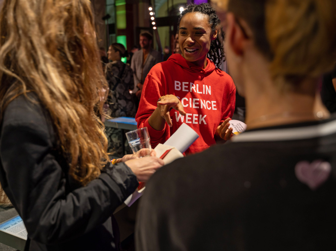 volunteer of the Berlin Science Week smiling at two guests at the Opening of the Berlin Science Week