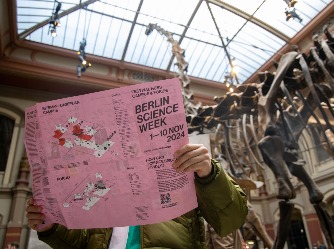 person reading the Berlin Science Week flyer in the dinosaur hall