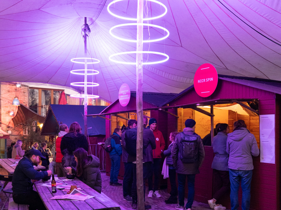 Evening view of the Tiny Galleries at Holzmarkt 25, illuminated by purple tube lights under a sail-shaped roof, as part of the Science & Culture FORUM