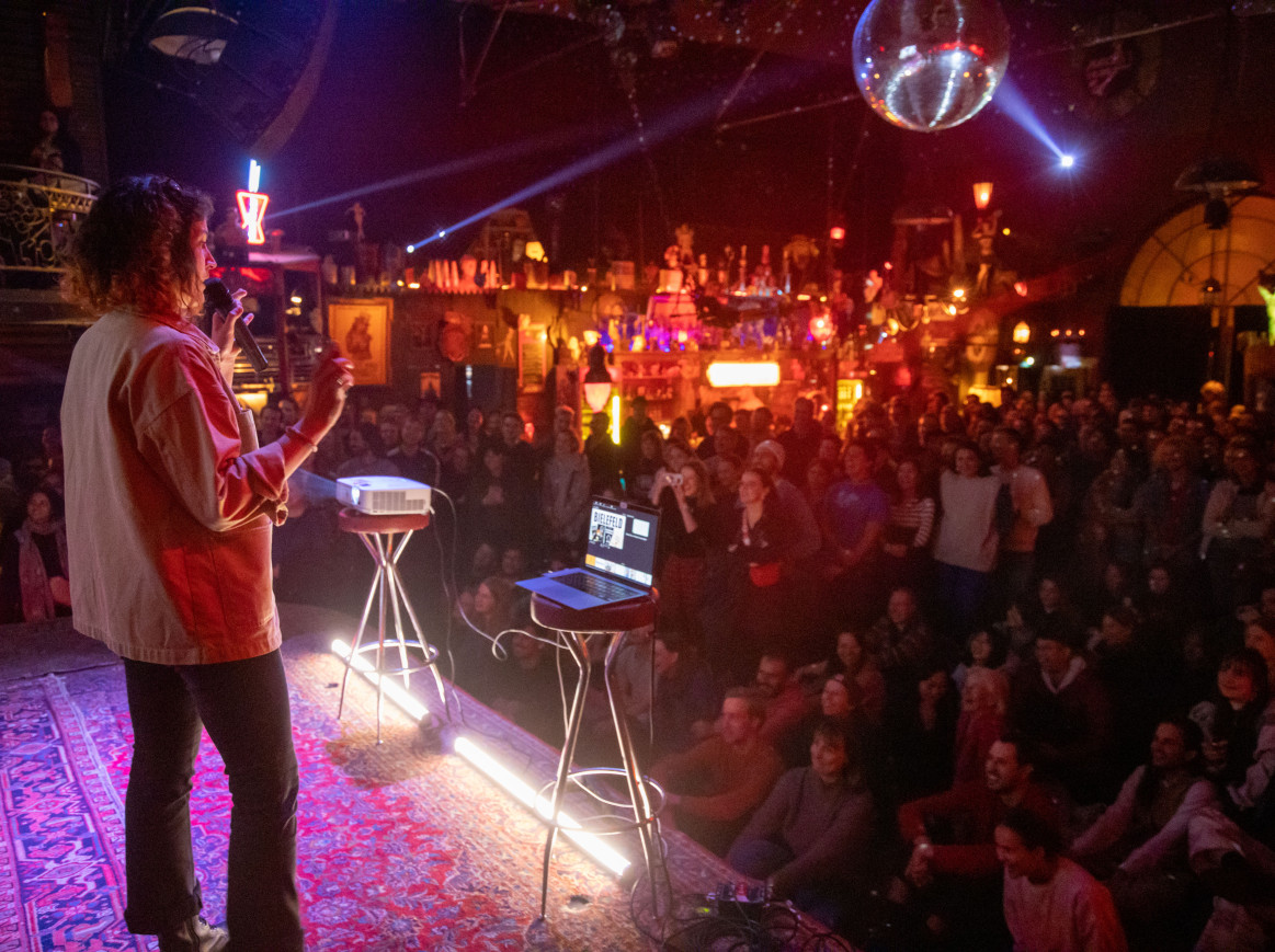 A scientist on stage discussing her work with the audience during a science slam at Roadrunners Paradise, organised by the Berlin Clusters of Excellence.